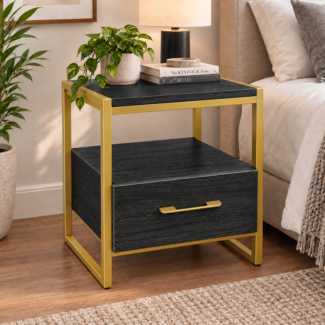 كمودينو LION HOME بمعدن ذهبي وخشب كونتر أسود مجزع ومقبض ذهبي بجوار سرير، مع درج ورف مفتوح.